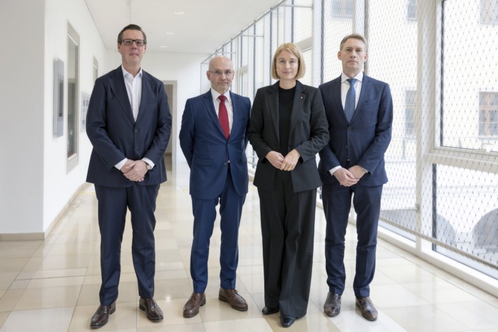 Vier Personen in dunklen Business-Outfits stehen in einem hellen Gang.