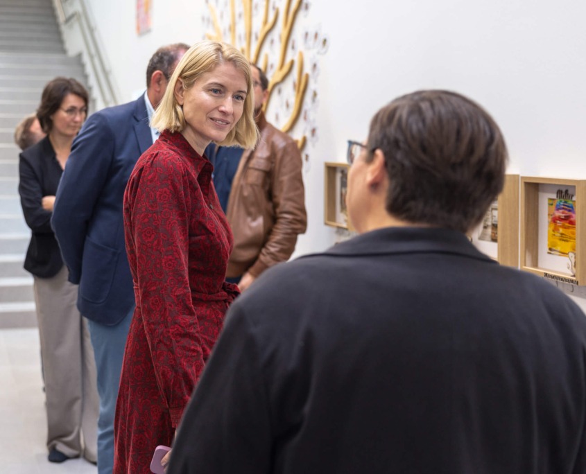 Gespräch zwischen zwei Personen in einer Bildungseinrichtung mit gerahmten Kinderarbeiten.