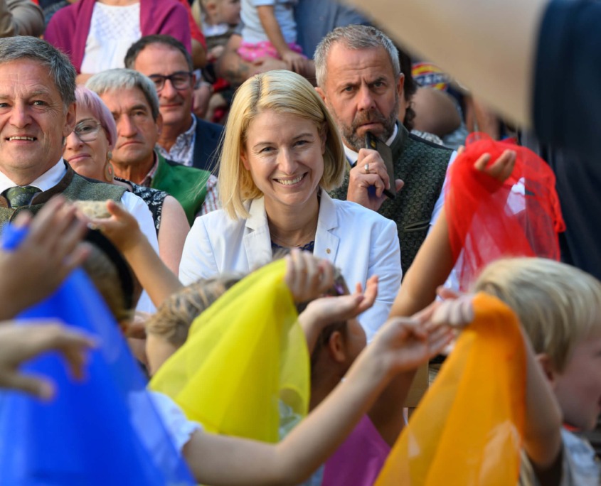 Kinder halten bunte Tücher bei einer Aufführung, Erwachsene sitzen im Publikum.